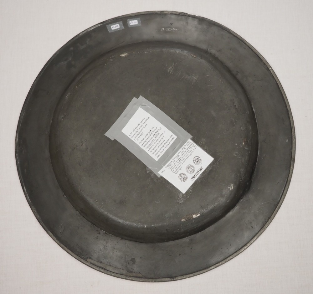 A circular seventeenth-century pewter charger plate with a plain rim featuring an engraved crest and stamped initials. View VII