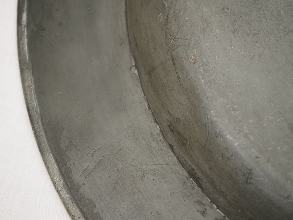 A circular seventeenth-century pewter charger plate with a plain rim featuring an engraved crest and stamped initials. View VIII