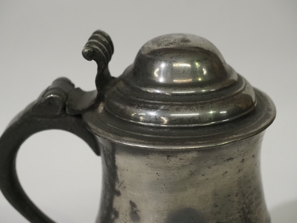 An 18th-century pewter pint tankard featuring a hinged dome lid, a curved scroll handle with a thumbpiece, and a moulded central band on a circular footed base. View III