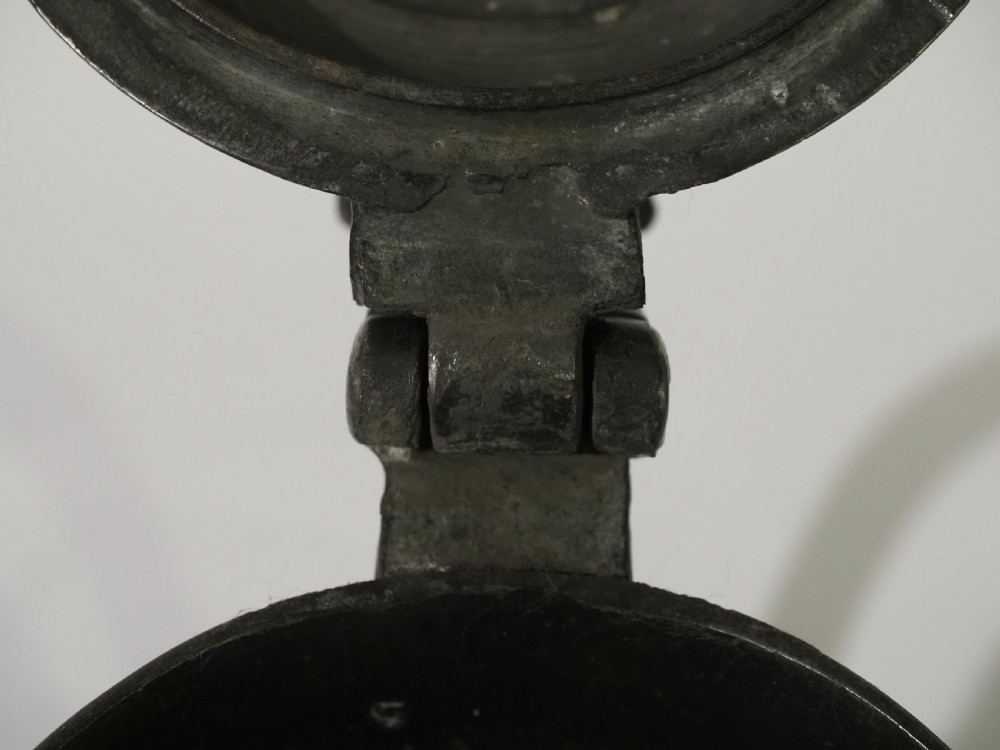 An 18th-century pewter pint tankard featuring a hinged dome lid, a curved scroll handle with a thumbpiece, and a moulded central band on a circular footed base. View VII