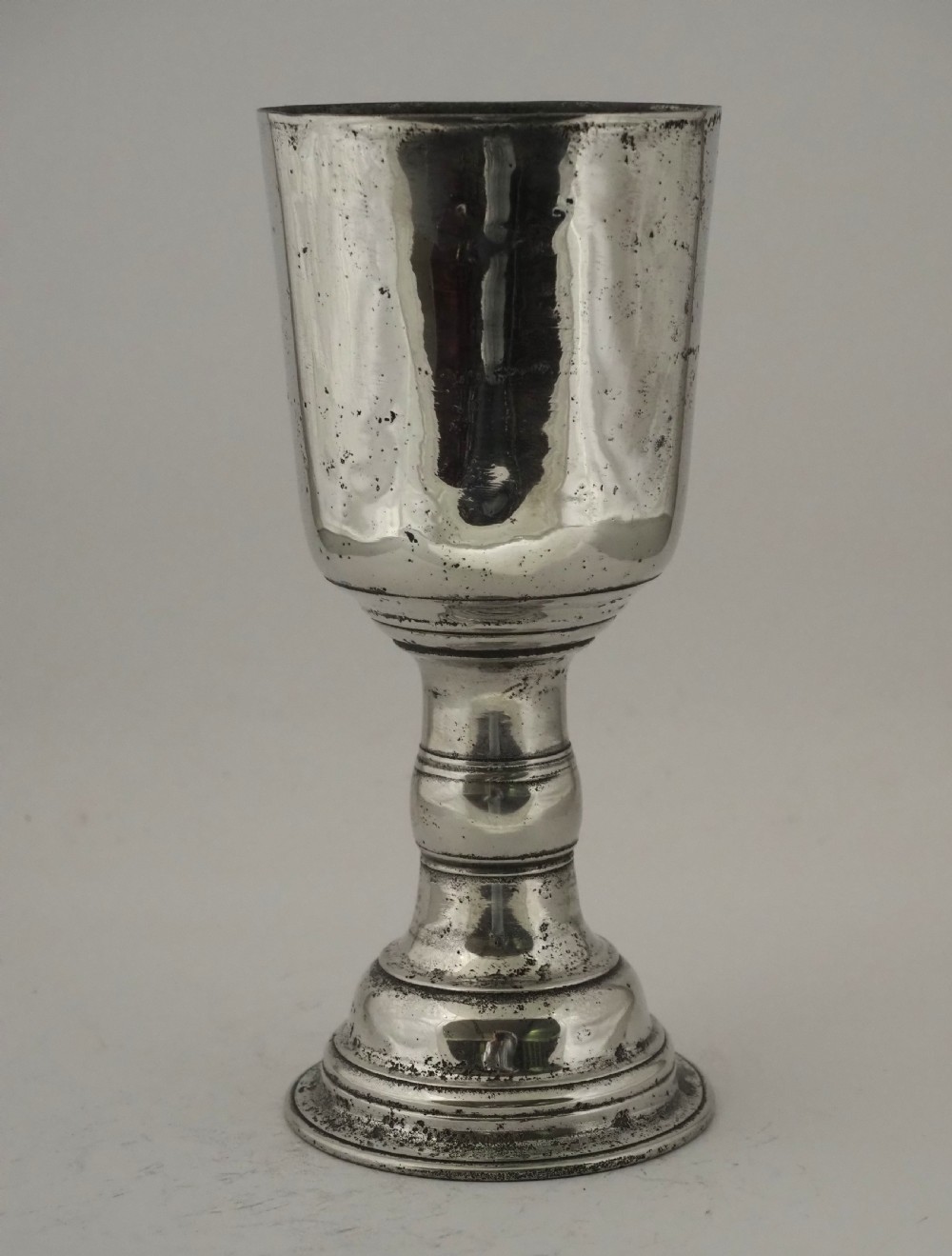 An antique Irish pewter chalice featuring a tall cylindrical bowl, a central knopped stem, and a stepped domed foot.