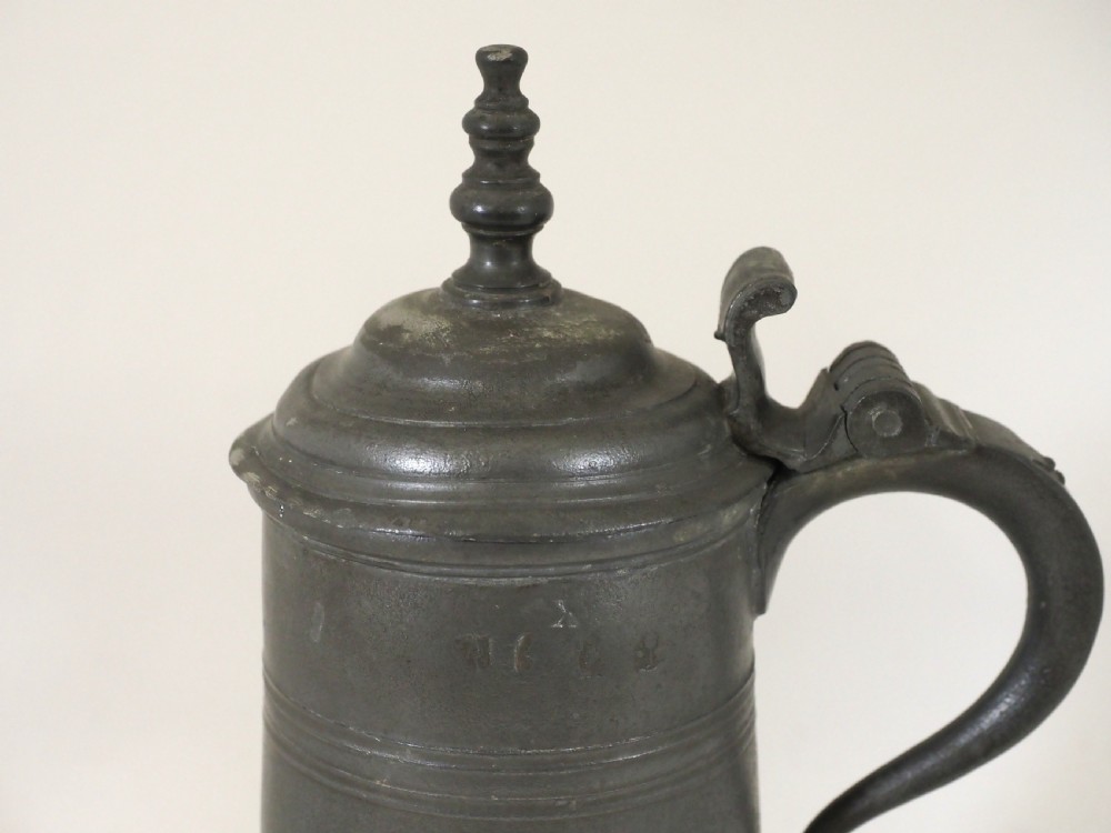 A dark grey early 18th-century English pewter spire flagon with a hinged lid, decorative spire finial, curved handle, and flared base. View II
