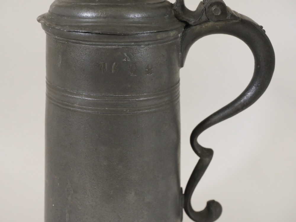 A dark grey early 18th-century English pewter spire flagon with a hinged lid, decorative spire finial, curved handle, and flared base. View III