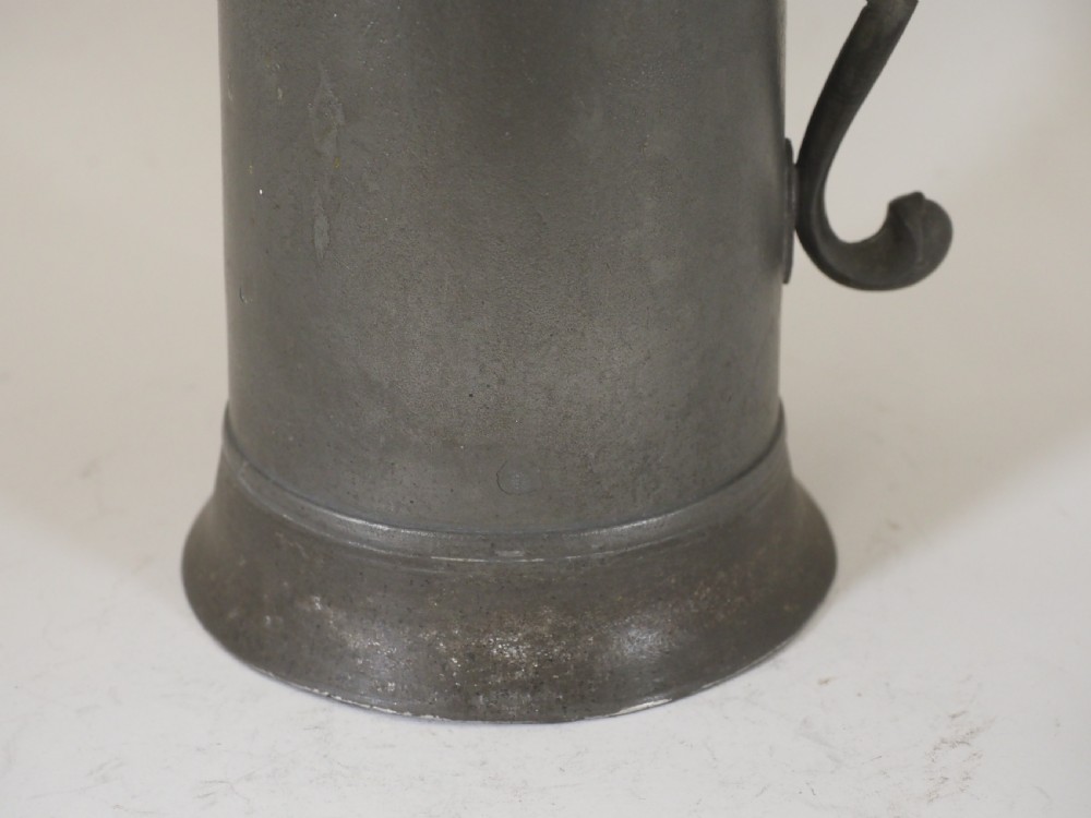 A dark grey early 18th-century English pewter spire flagon with a hinged lid, decorative spire finial, curved handle, and flared base. View IV