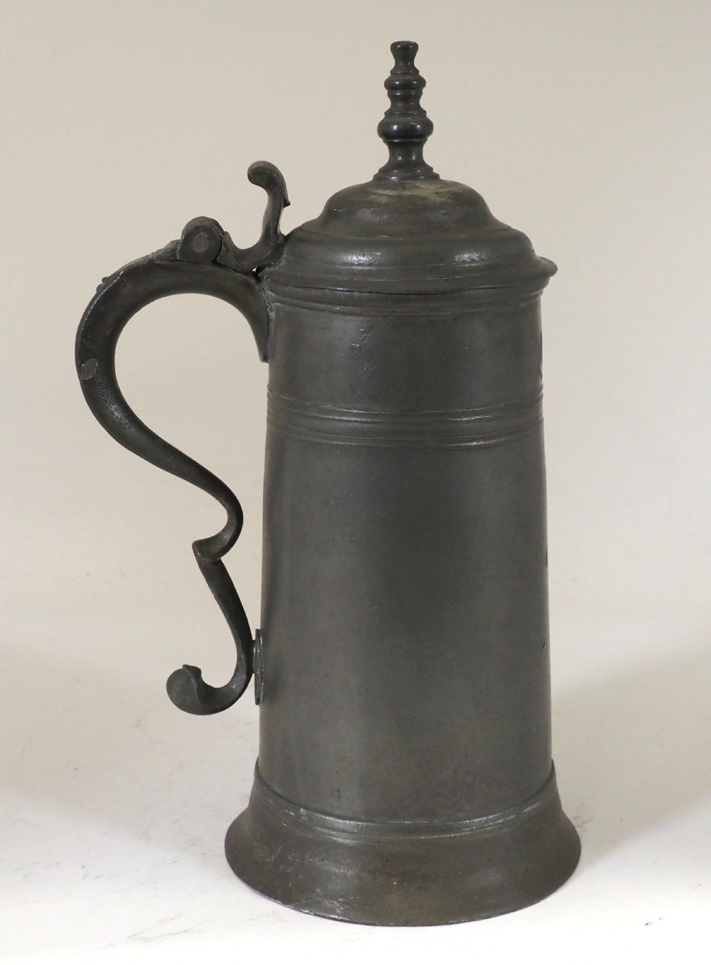 A dark grey early 18th-century English pewter spire flagon with a hinged lid, decorative spire finial, curved handle, and flared base. View VII