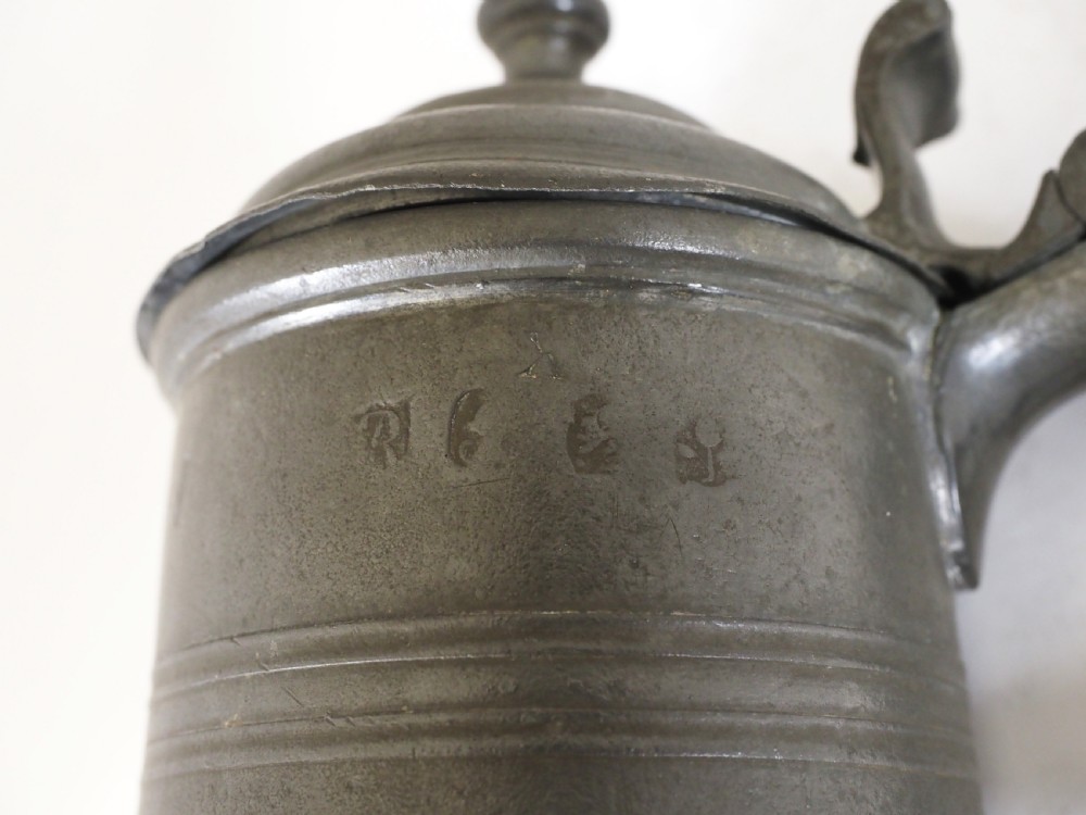 A dark grey early 18th-century English pewter spire flagon with a hinged lid, decorative spire finial, curved handle, and flared base. View IX