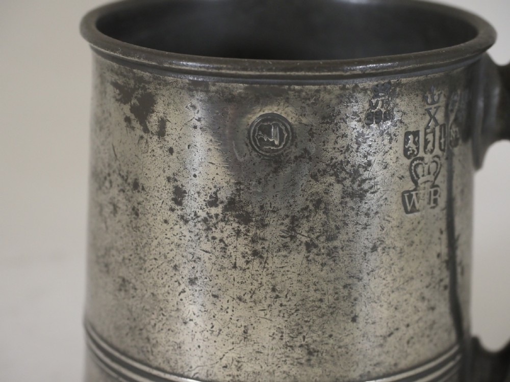 A cylindrical pewter pint measure featuring a curved handle, horizontal molded bands around the base, and stamped verification marks near the upper rim. View III