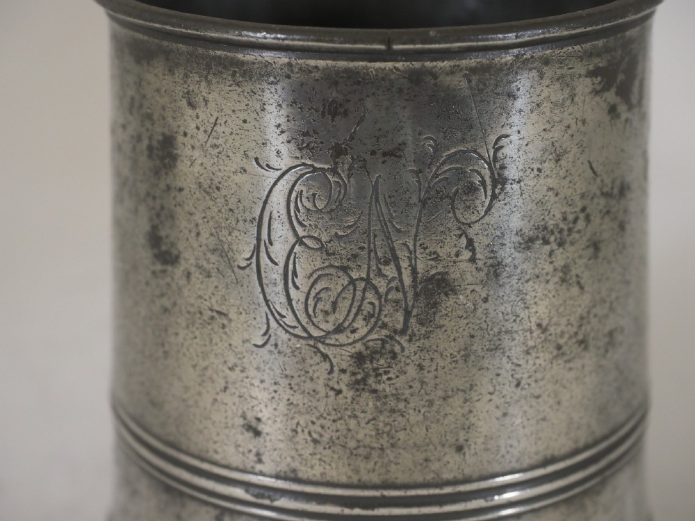 A cylindrical pewter pint measure featuring a curved handle, horizontal molded bands around the base, and stamped verification marks near the upper rim. View IV