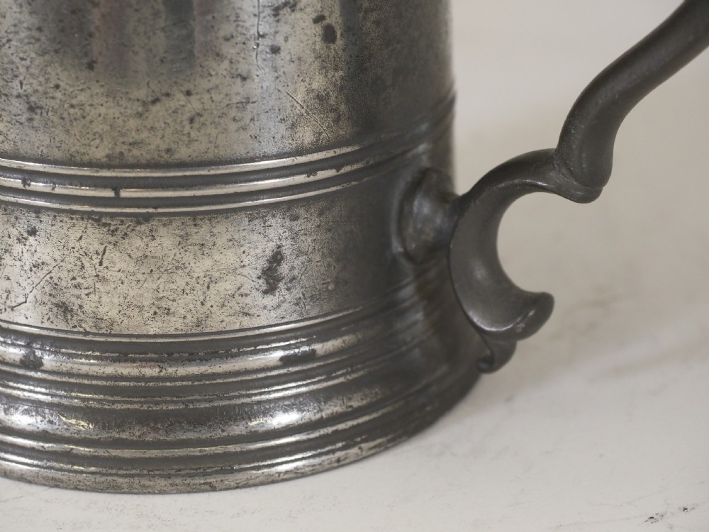 A cylindrical pewter pint measure featuring a curved handle, horizontal molded bands around the base, and stamped verification marks near the upper rim. View VI