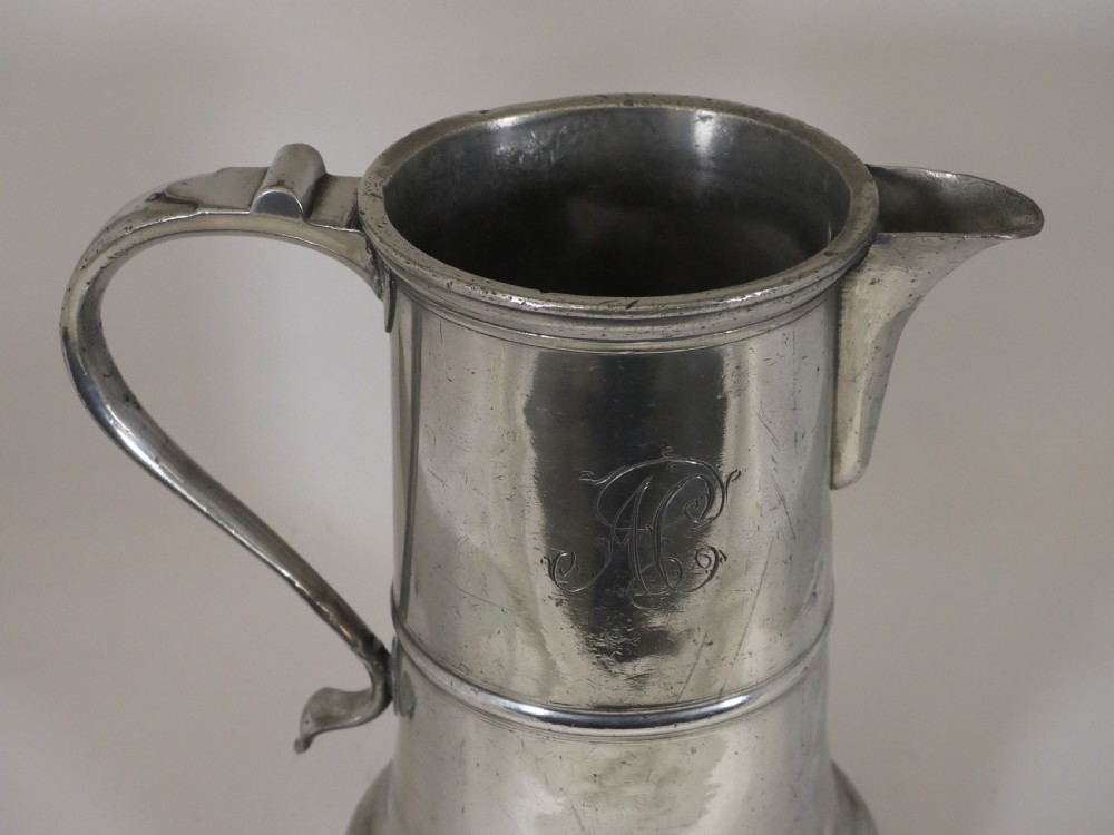 An 18th-century English pewter ale jug featuring a flared base, central girdle moulding, single poured spout, and curved handle. View IX