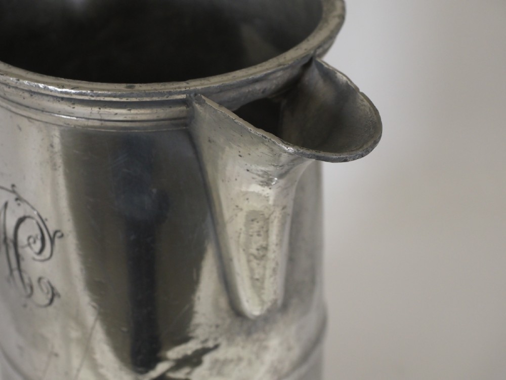 An 18th-century English pewter ale jug featuring a flared base, central girdle moulding, single poured spout, and curved handle. View X