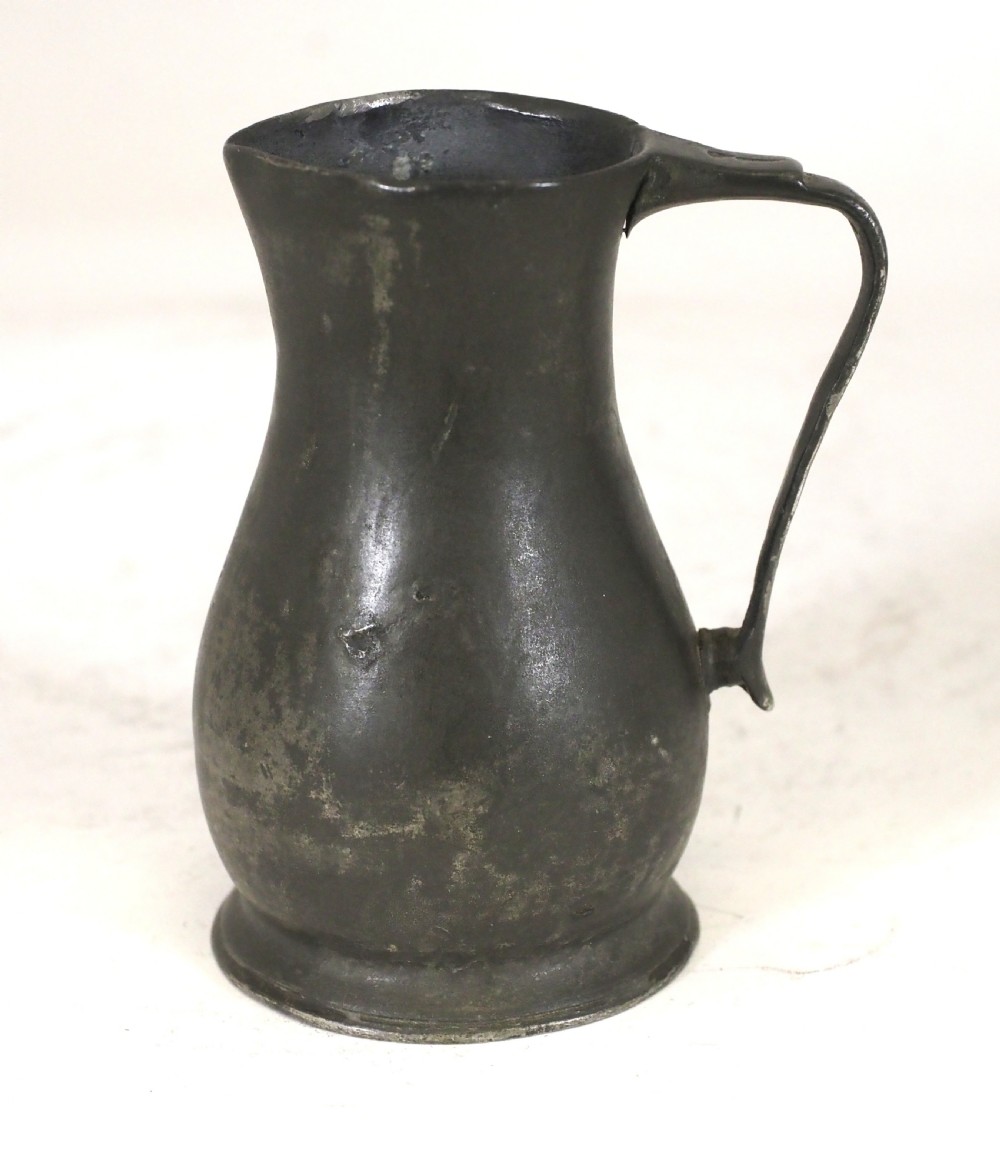 An antique dark grey pewter lidless baluster measure featuring a curved handle and flared rim.