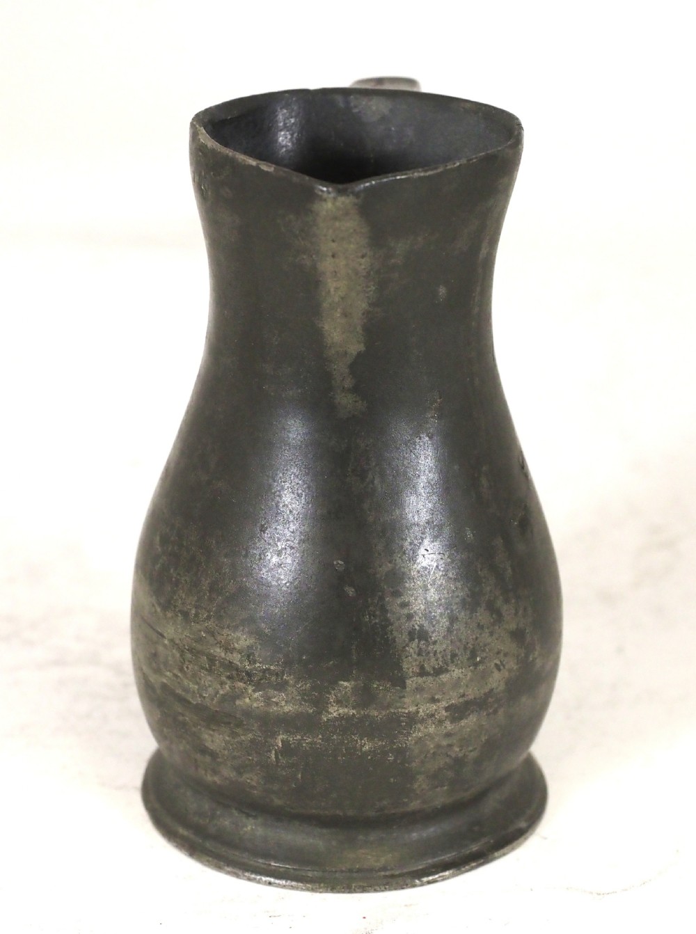 An antique dark grey pewter lidless baluster measure featuring a curved handle and flared rim. View II