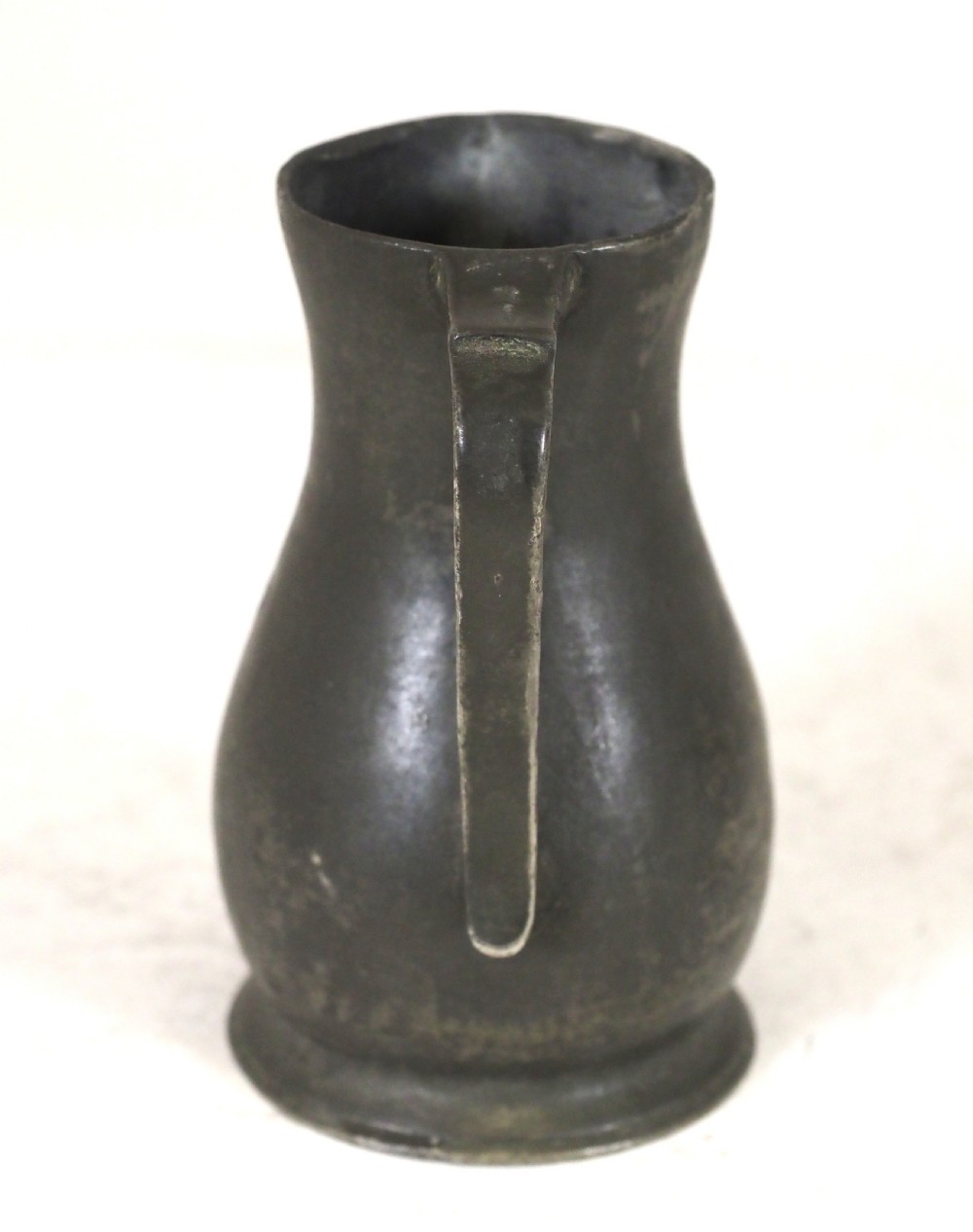 An antique dark grey pewter lidless baluster measure featuring a curved handle and flared rim. View IV
