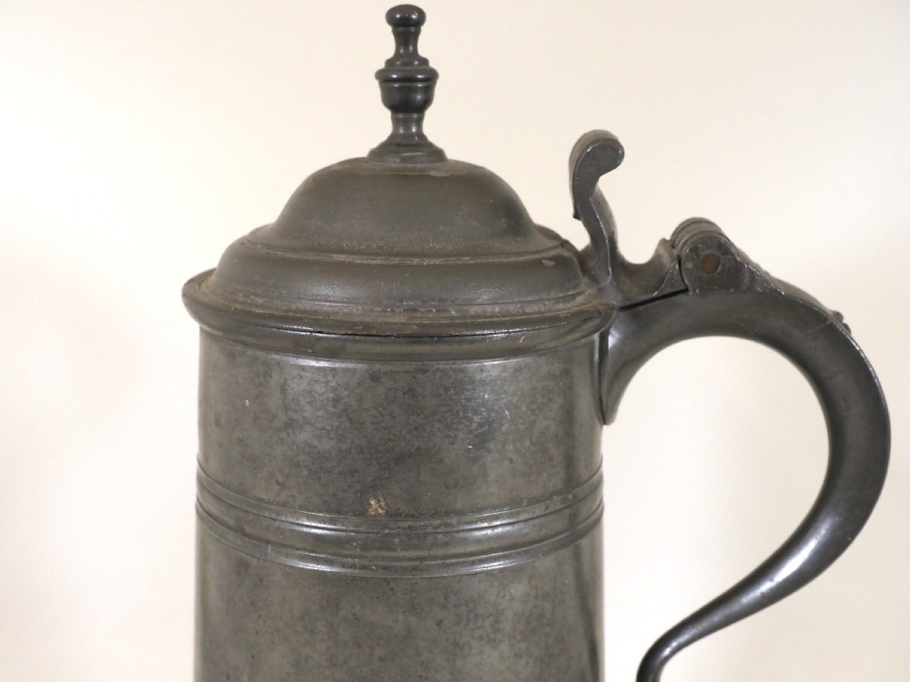 An eighteenth-century dark grey pewter spire flagon featuring a tapered cylindrical body, domed lid with spire finial, double-scroll handle, and moulded spreading base. View II