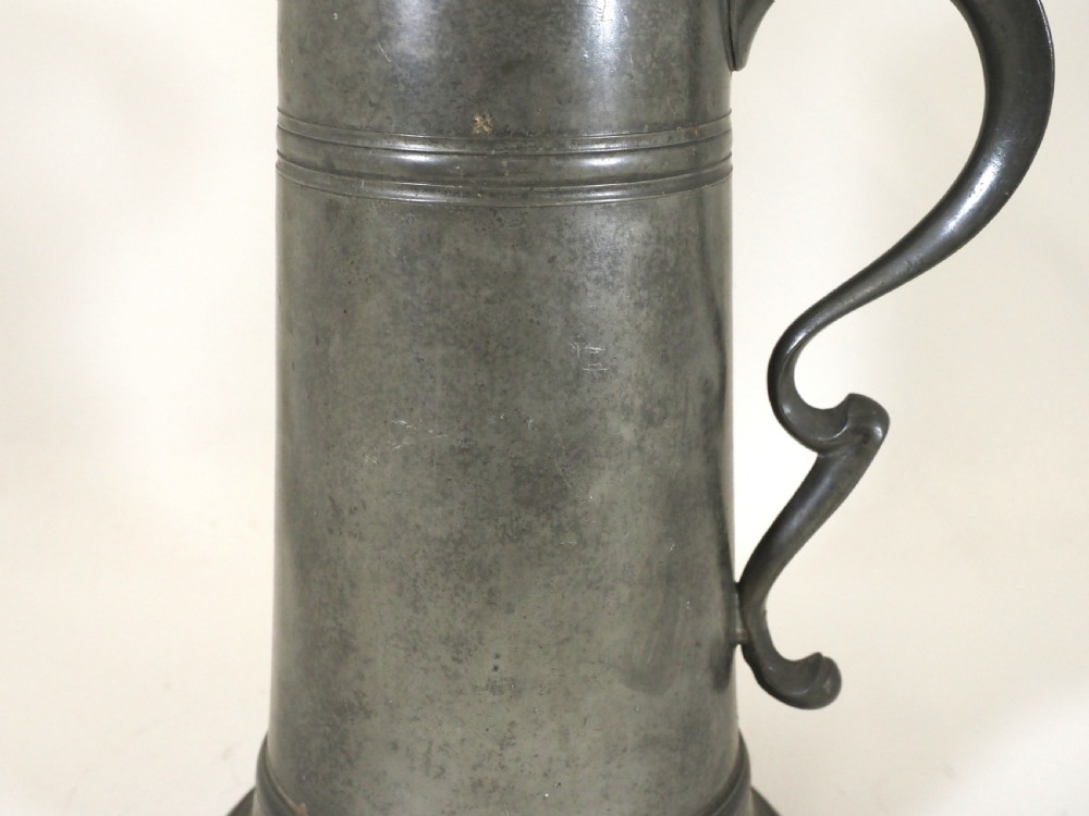 An eighteenth-century dark grey pewter spire flagon featuring a tapered cylindrical body, domed lid with spire finial, double-scroll handle, and moulded spreading base. View III