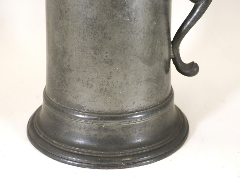An eighteenth-century dark grey pewter spire flagon featuring a tapered cylindrical body, domed lid with spire finial, double-scroll handle, and moulded spreading base. View IV