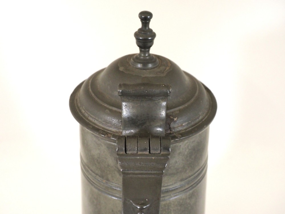 An eighteenth-century dark grey pewter spire flagon featuring a tapered cylindrical body, domed lid with spire finial, double-scroll handle, and moulded spreading base. View V