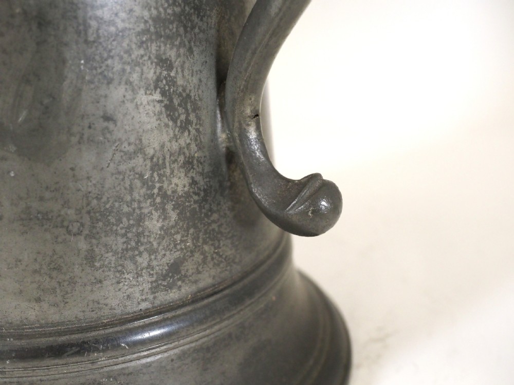 An eighteenth-century dark grey pewter spire flagon featuring a tapered cylindrical body, domed lid with spire finial, double-scroll handle, and moulded spreading base. View VI