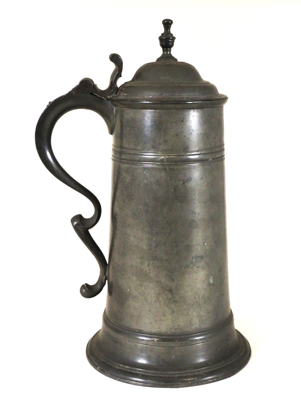 An eighteenth-century dark grey pewter spire flagon featuring a tapered cylindrical body, domed lid with spire finial, double-scroll handle, and moulded spreading base. View IX