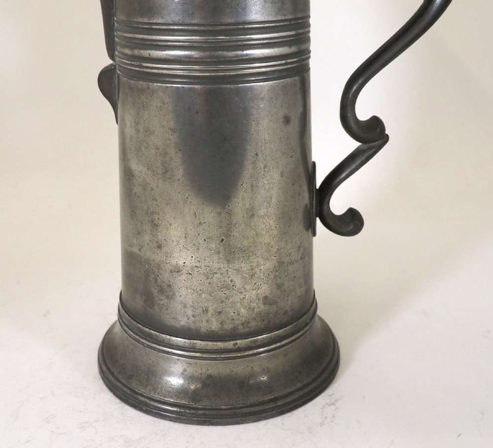 An antique late 18th-century spouted pewter spire flagon featuring a double-scroll handle, domed lid, and flared circular base. View III