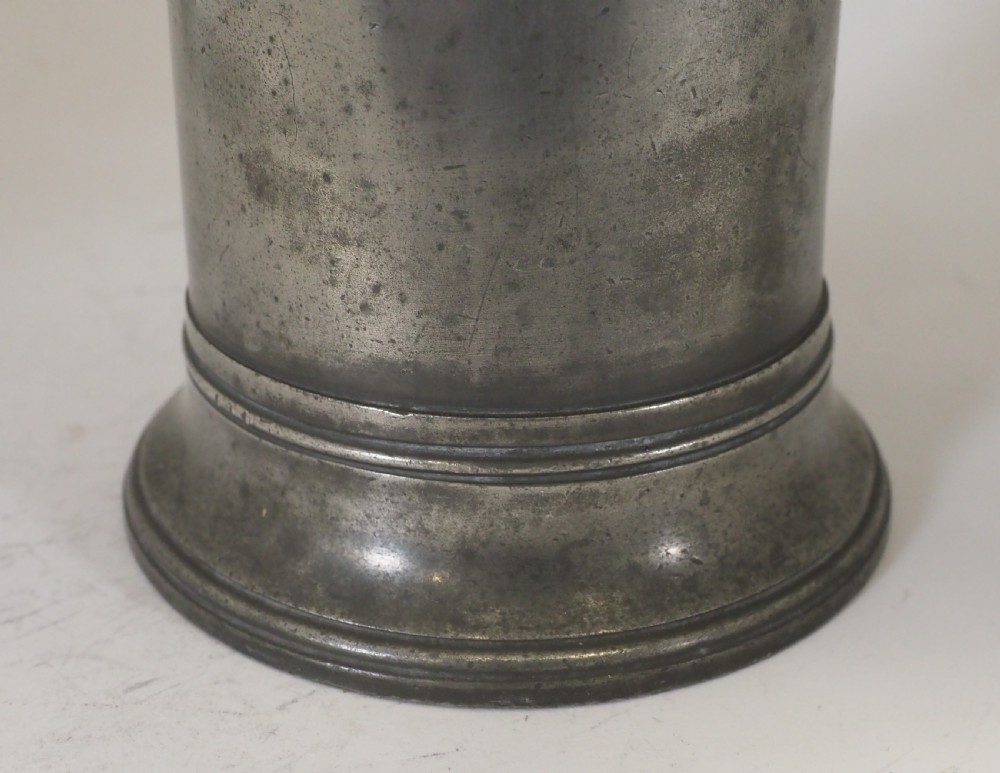 An antique late 18th-century spouted pewter spire flagon featuring a double-scroll handle, domed lid, and flared circular base. View V