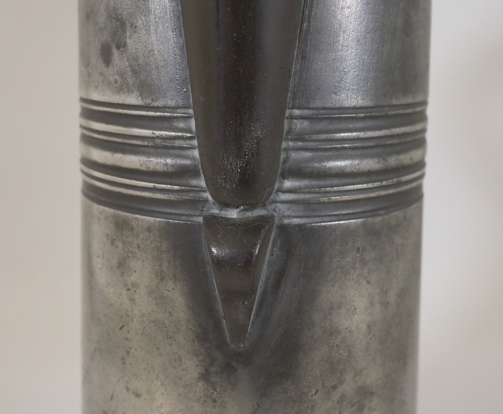 An antique late 18th-century spouted pewter spire flagon featuring a double-scroll handle, domed lid, and flared circular base. View VI