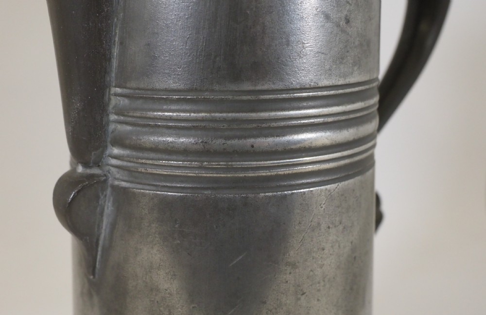 An antique late 18th-century spouted pewter spire flagon featuring a double-scroll handle, domed lid, and flared circular base. View VII