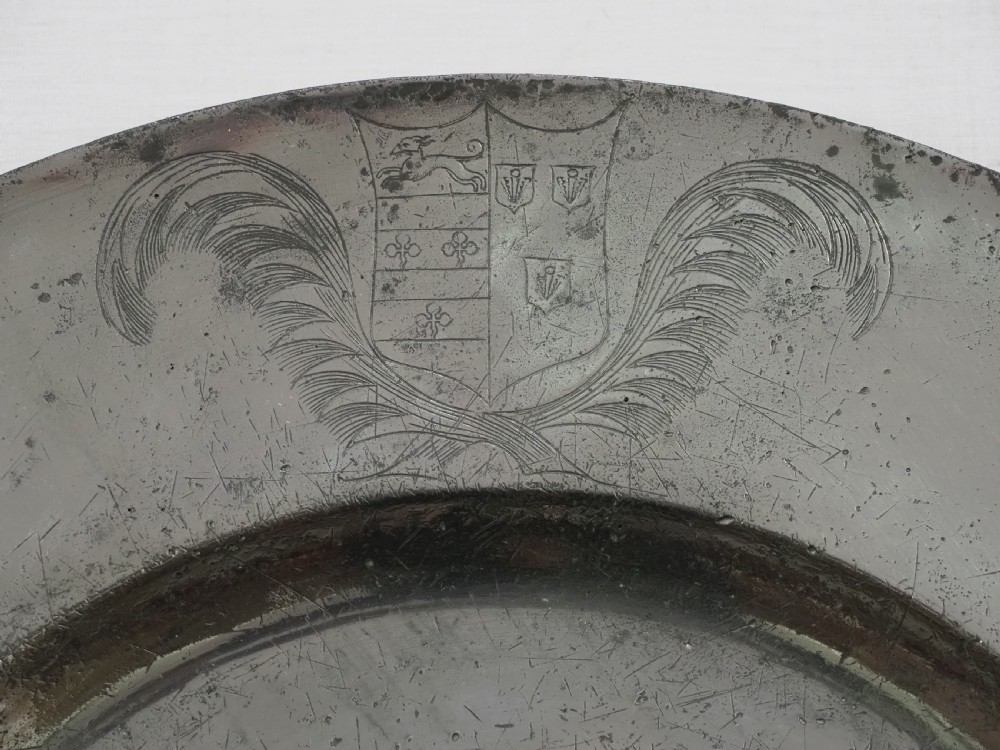A circular seventeenth-century pewter broad rim charger featuring an engraved coat of arms flanked by feathered plumes on the upper rim. View II