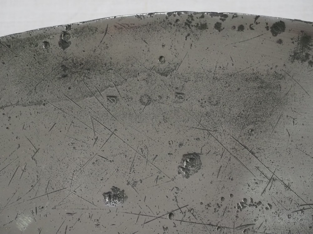 A circular seventeenth-century pewter broad rim charger featuring an engraved coat of arms flanked by feathered plumes on the upper rim. View III