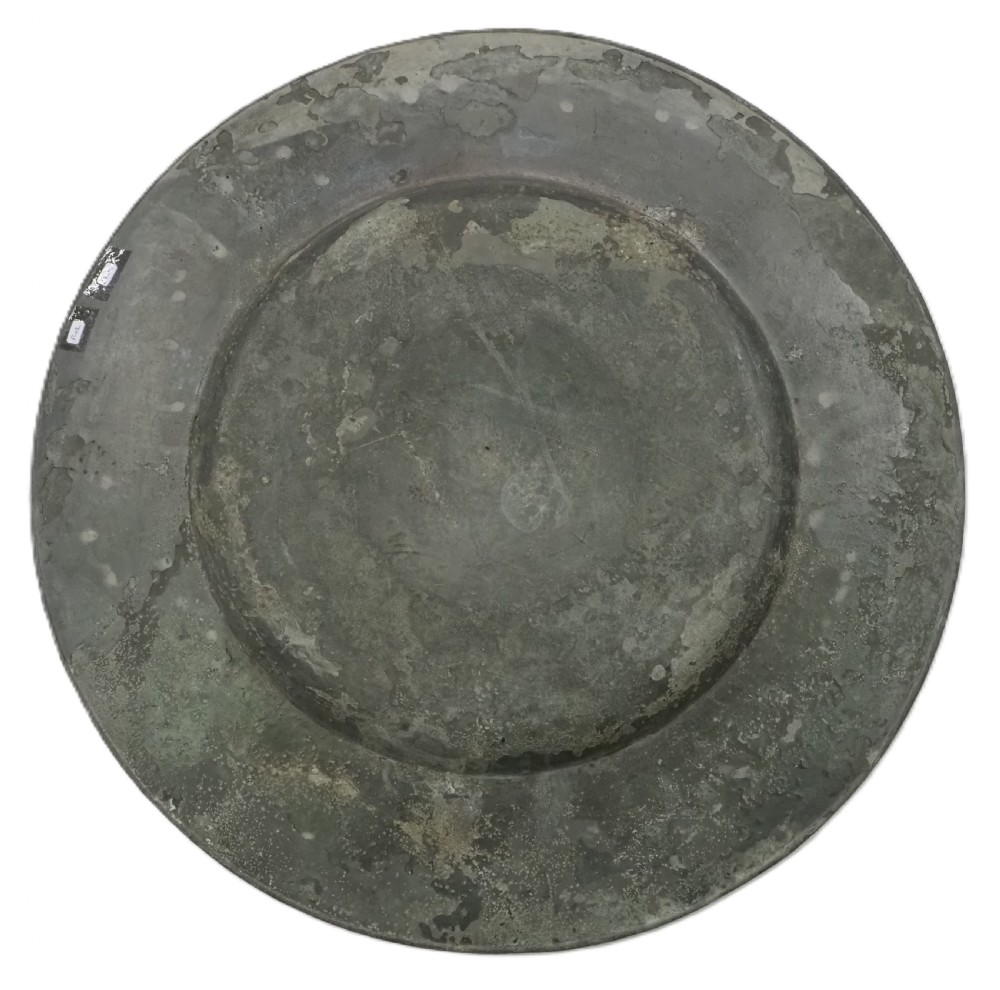 A circular seventeenth-century pewter broad rim charger featuring an engraved coat of arms flanked by feathered plumes on the upper rim. View IV