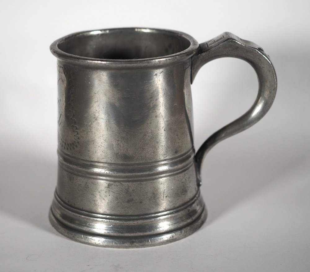 An antique grey pewter pint measure featuring a curved handle, cylindrical body with moulded bands, and engraved lettering on the side.