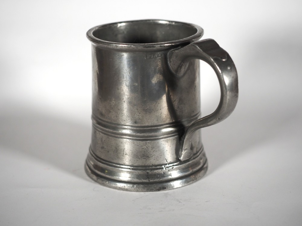 An antique grey pewter pint measure featuring a curved handle, cylindrical body with moulded bands, and engraved lettering on the side. View II