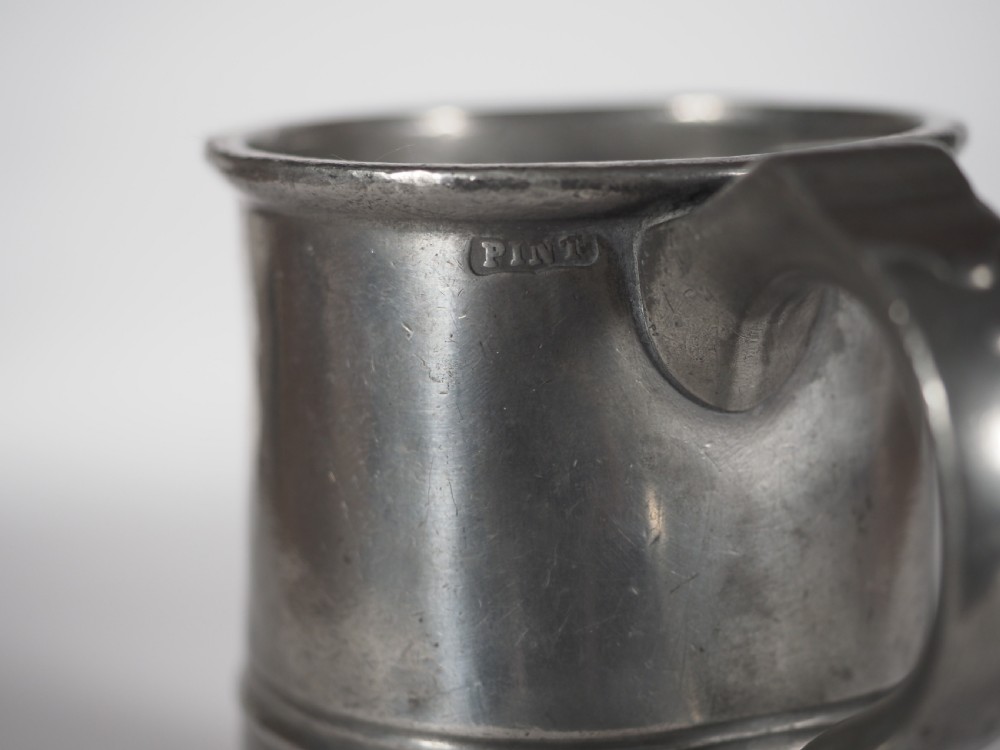 An antique grey pewter pint measure featuring a curved handle, cylindrical body with moulded bands, and engraved lettering on the side. View IV