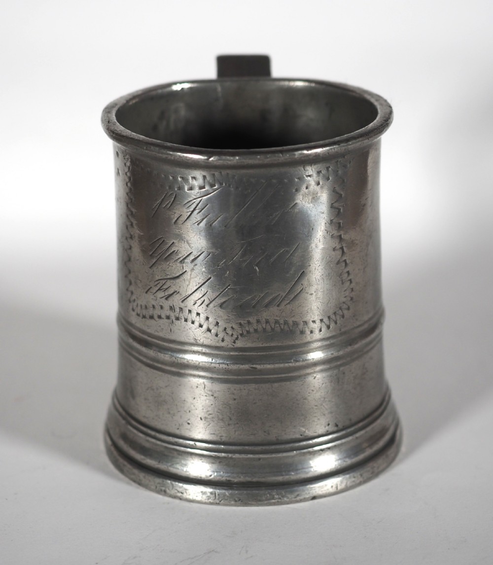 An antique grey pewter pint measure featuring a curved handle, cylindrical body with moulded bands, and engraved lettering on the side. View V