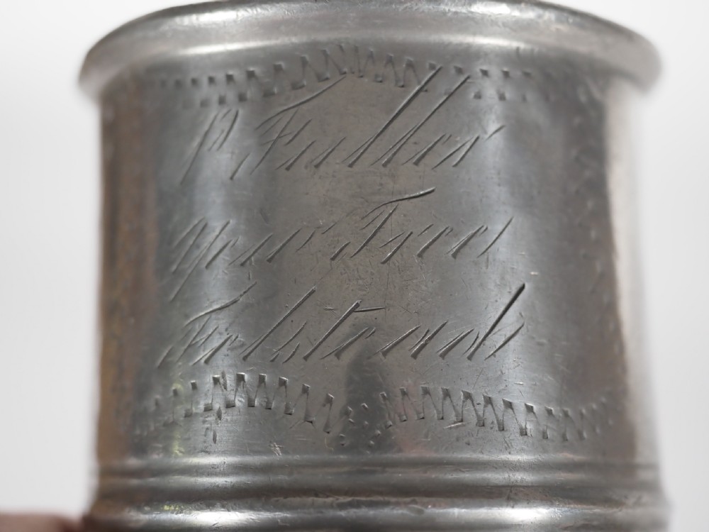 An antique grey pewter pint measure featuring a curved handle, cylindrical body with moulded bands, and engraved lettering on the side. View VII