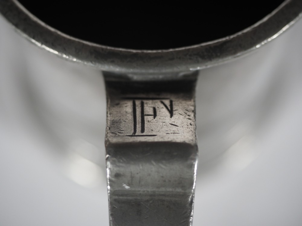 An antique grey pewter pint measure featuring a curved handle, cylindrical body with moulded bands, and engraved lettering on the side. View IX