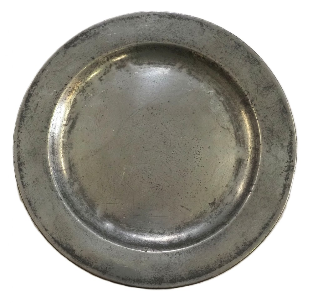 An 18th-century circular English pewter plate featuring a wide plain rim and aged grey metal patination.