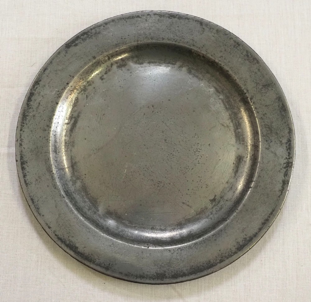 An 18th-century circular English pewter plate featuring a wide plain rim and aged grey metal patination. View II