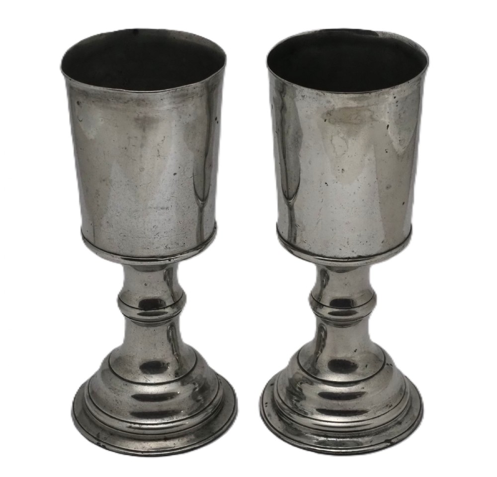 A pair of Georgian pewter chalices featuring cylindrical bowls, knopped stems, and stepped circular bases.