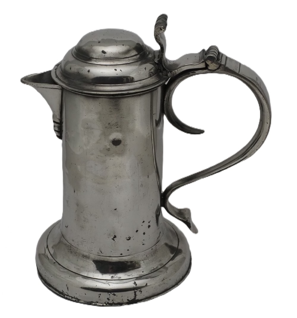 An 18th-century Irish pewter church flagon with a domed hinged lid, thumbpiece, curved handle, and broad flared base.