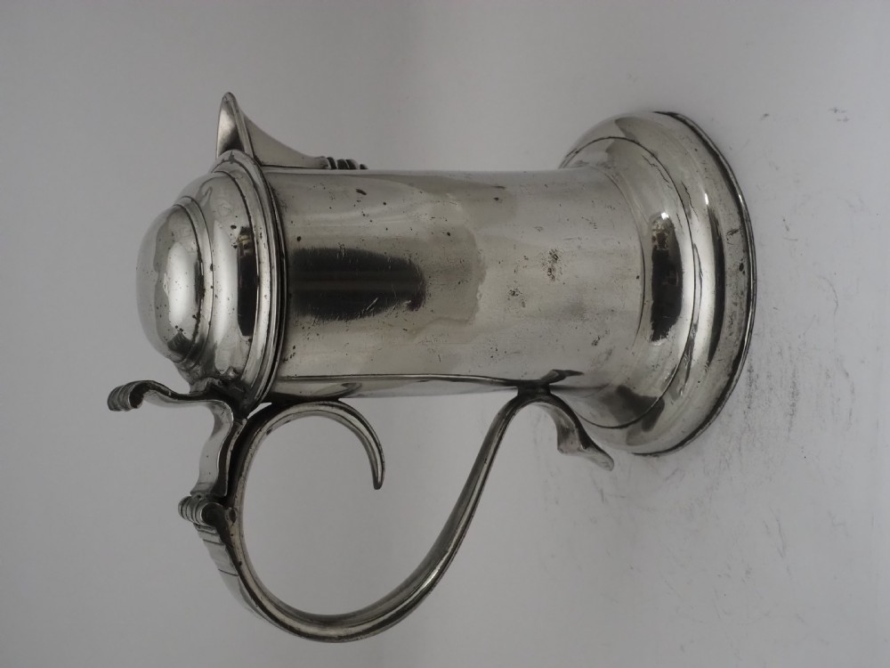An 18th-century Irish pewter church flagon with a domed hinged lid, thumbpiece, curved handle, and broad flared base. View IV