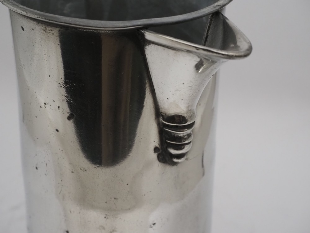 An 18th-century Irish pewter church flagon with a domed hinged lid, thumbpiece, curved handle, and broad flared base. View VI