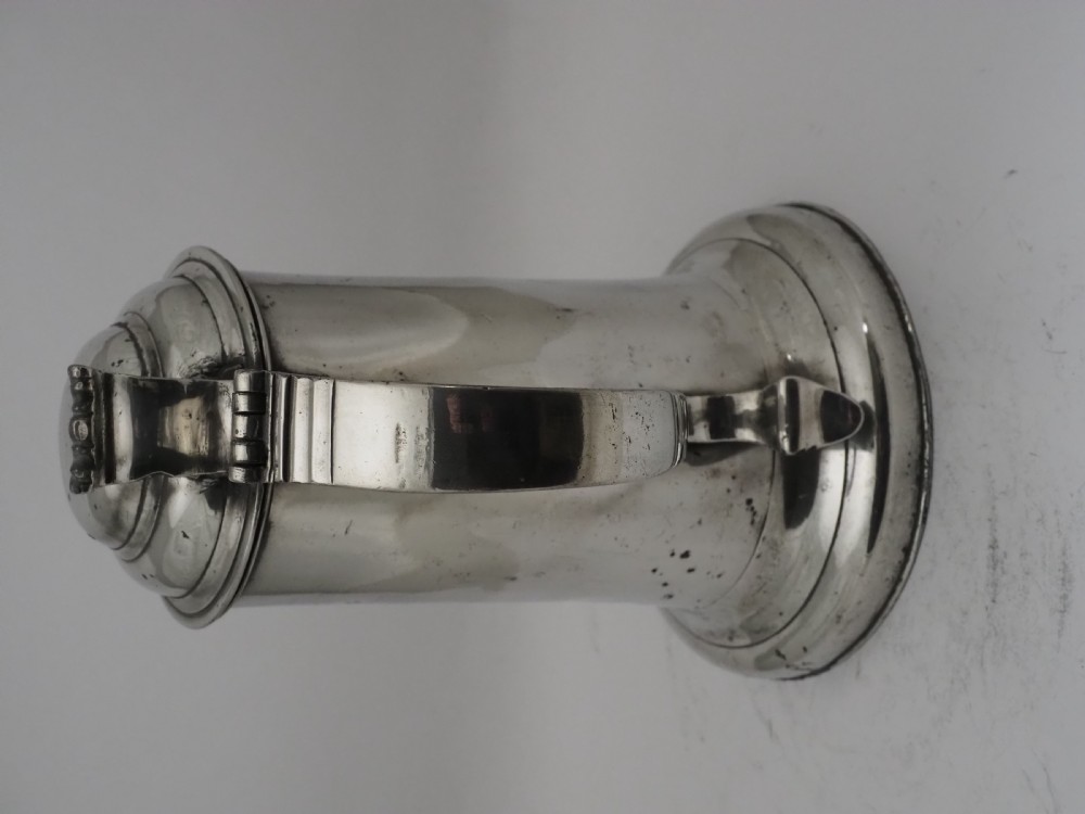 An 18th-century Irish pewter church flagon with a domed hinged lid, thumbpiece, curved handle, and broad flared base. View X