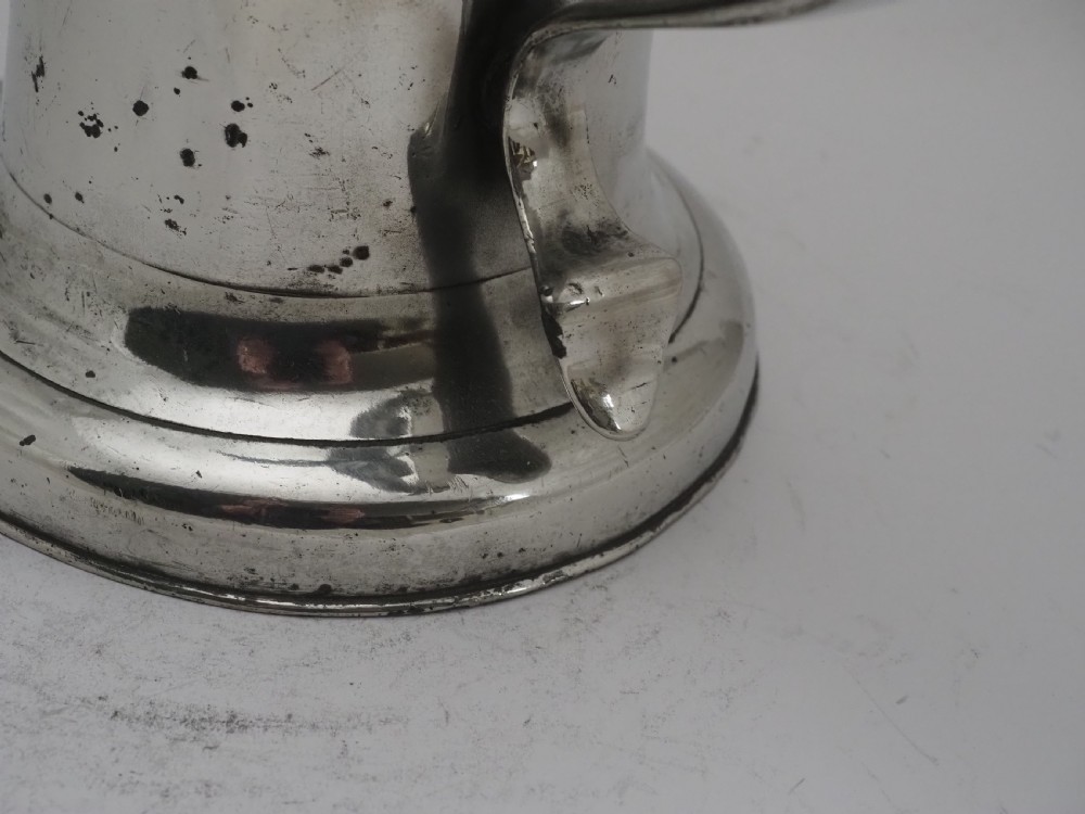 An 18th-century Irish pewter church flagon with a domed hinged lid, thumbpiece, curved handle, and broad flared base. View XII