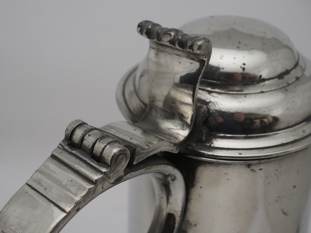 An 18th-century Irish pewter church flagon with a domed hinged lid, thumbpiece, curved handle, and broad flared base. View XIV
