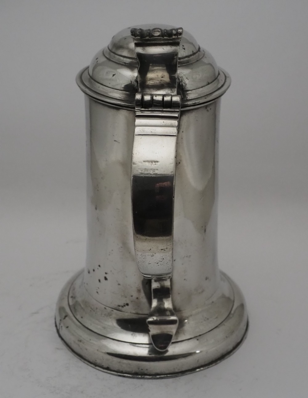An 18th-century Irish pewter church flagon with a domed hinged lid, thumbpiece, curved handle, and broad flared base. View XV