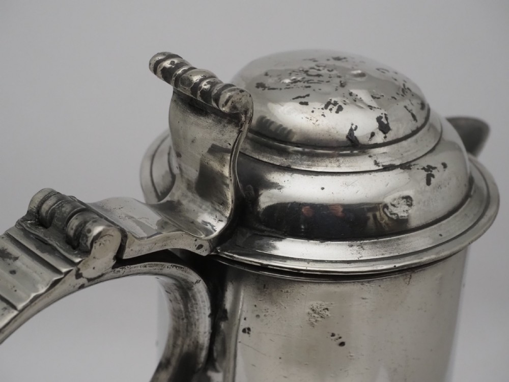 An 18th-century Georgian Irish pewter church flagon featuring a domed hinged lid, double-scroll handle, spout, and circular moulded base. View IX