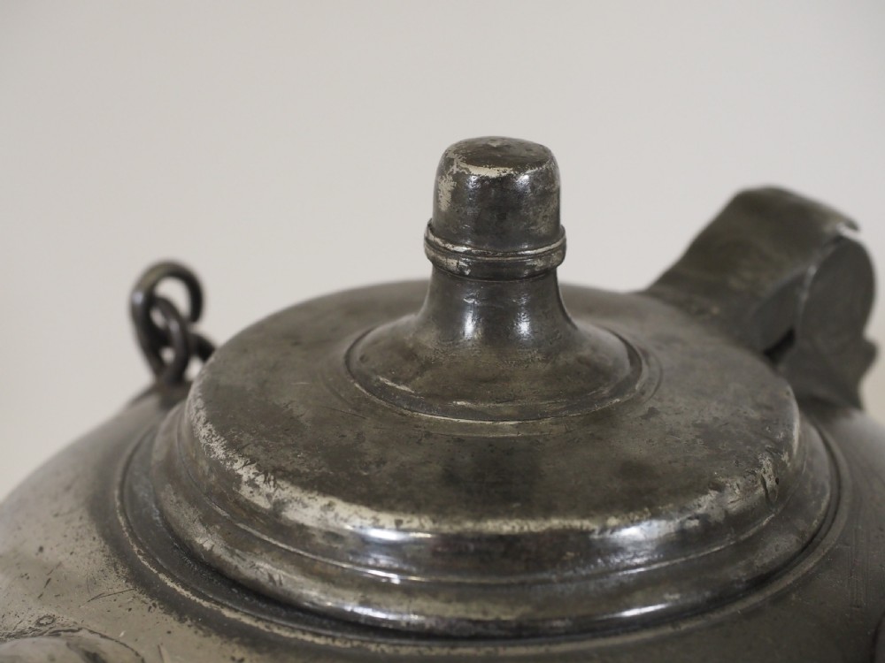An antique 18th-century Swiss pewter biberon water vessel featuring a flared base, side spout with relief detailing, fitted lid, and tall wire handle. View VI