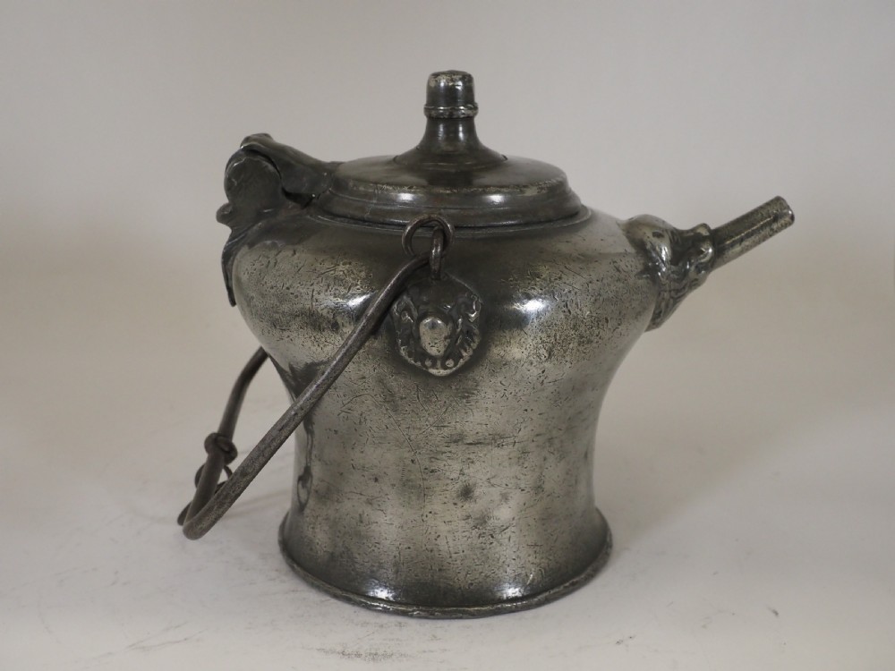 An antique 18th-century Swiss pewter biberon water vessel featuring a flared base, side spout with relief detailing, fitted lid, and tall wire handle. View X